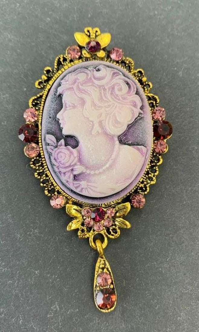 Silhouetted Purple Cameo Brooch: Silhouetted Purple Cameo Brooch This beautiful silhouetted purple cameo brooch features intricate metal carvings framing the portrait and shimmering purple and pink gemstone accents throughout. A