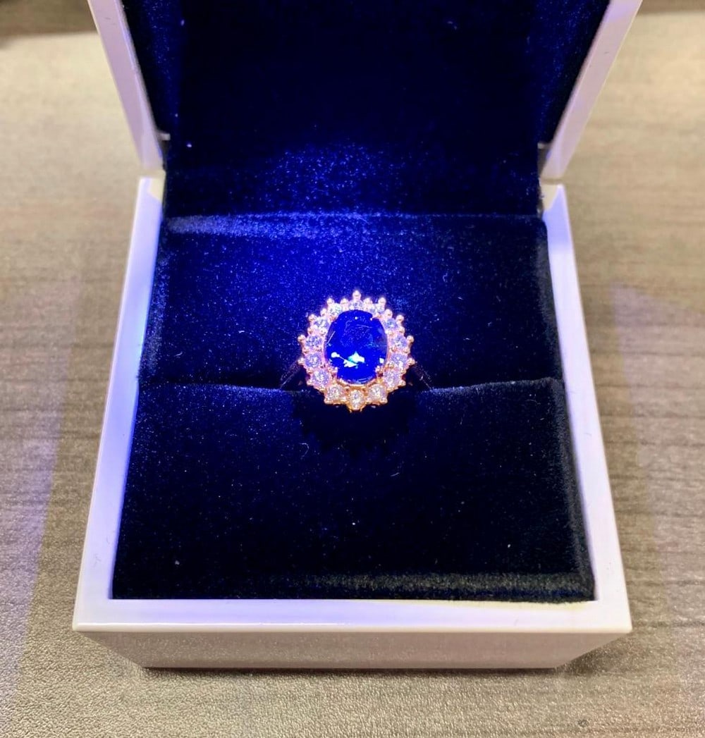 Lady Diana Blue Sapphire Yellow Gold Cluster Ring: A Lady Diana Blue Sapphire 14kt Yellow Gold Plated Cluster Ring. The Ring Displays a Cluster Of Simulated Diamonds Around A Oval Cut Blue Sapphire. The Ring Is Crafted With Precision & An Excellent Co