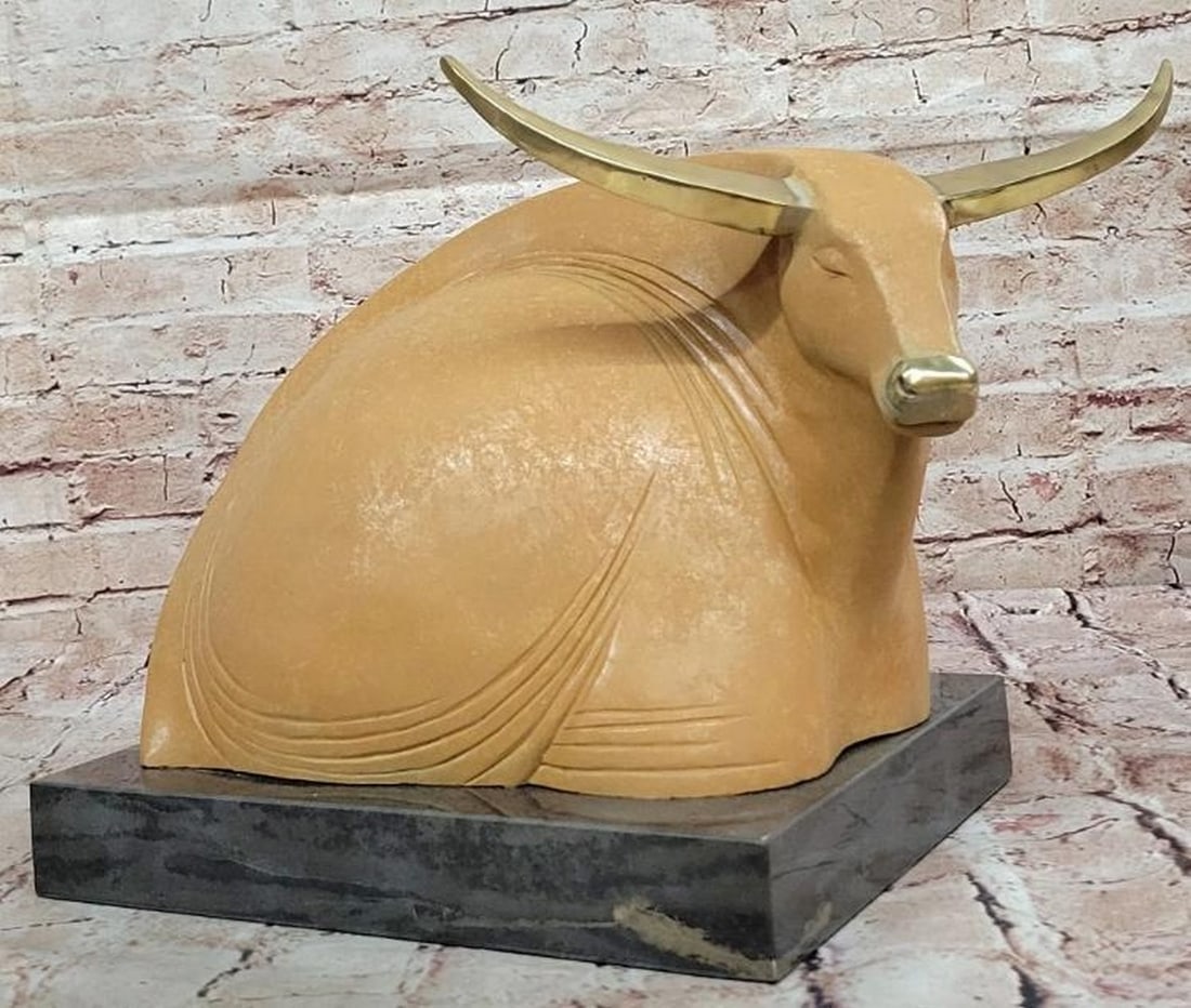 Serene Strength: Abstract Bronze Bull Reclining with Gold Patina Accents: Serene Strength: Abstract Bronze Bull Reclining with Gold Patina Accents This captivating bronze reproduction sculpture presents an abstract bull reclining in peaceful repose, its eyes gently closed