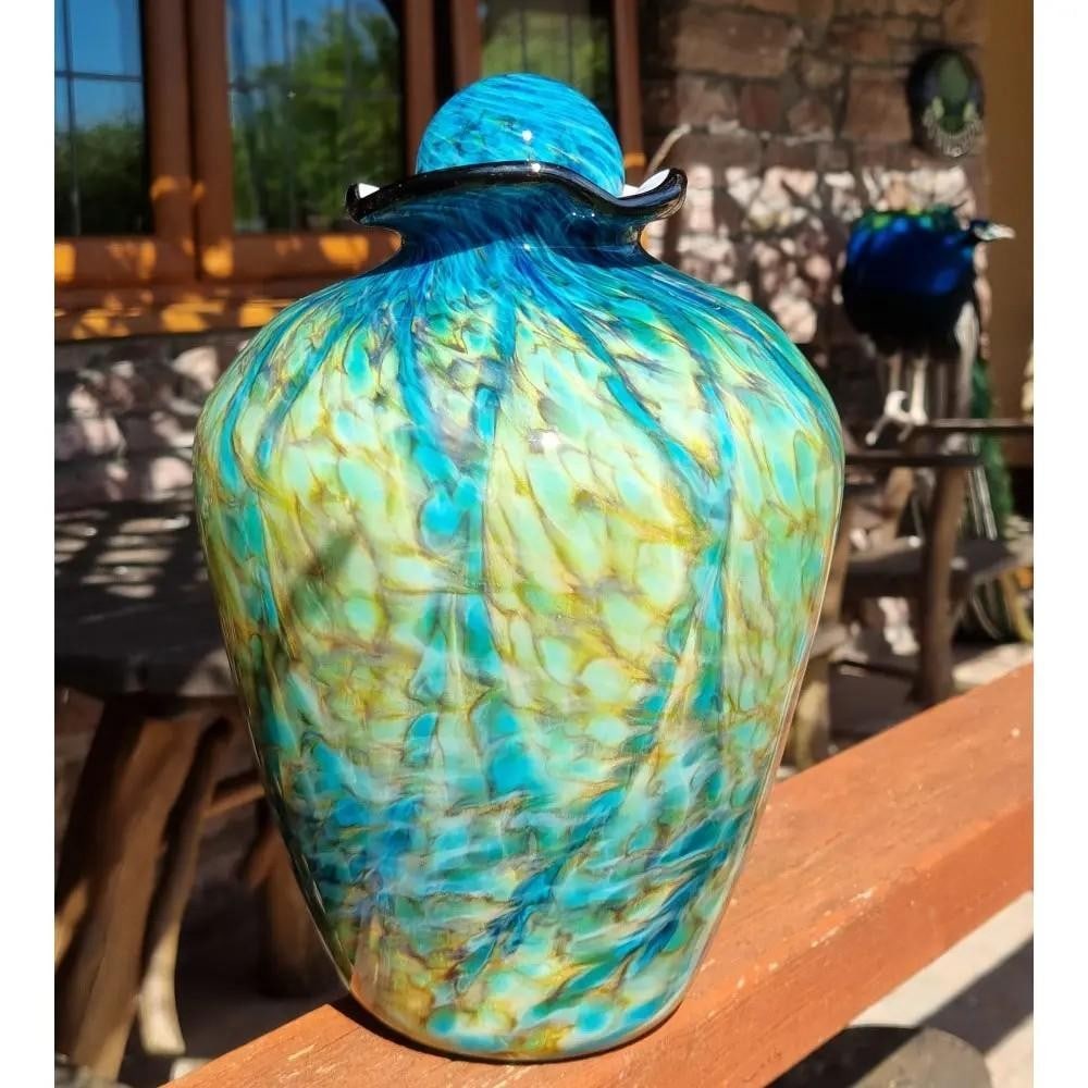Bella' Hand Blown Glass Urn: 'Bella' Hand Blown Glass Urn This is a beautiful hand-blown glass urn, aptly named "Bella." Crafted with intricate detail, its swirling patterns of turquoise, gold, and green create a