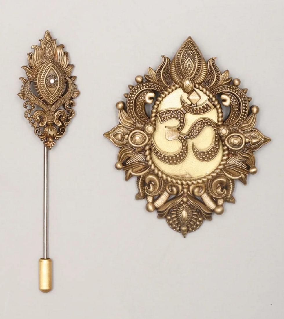 Sacred Om & Trayambakam Brooch and Pin Set: Sacred Om & Trayambakam Brooch and Pin Set This lapel pin and brooch set is a refined way to express faith and elegance. Crafted from brass, both pieces feature intricate designs that blend spirit