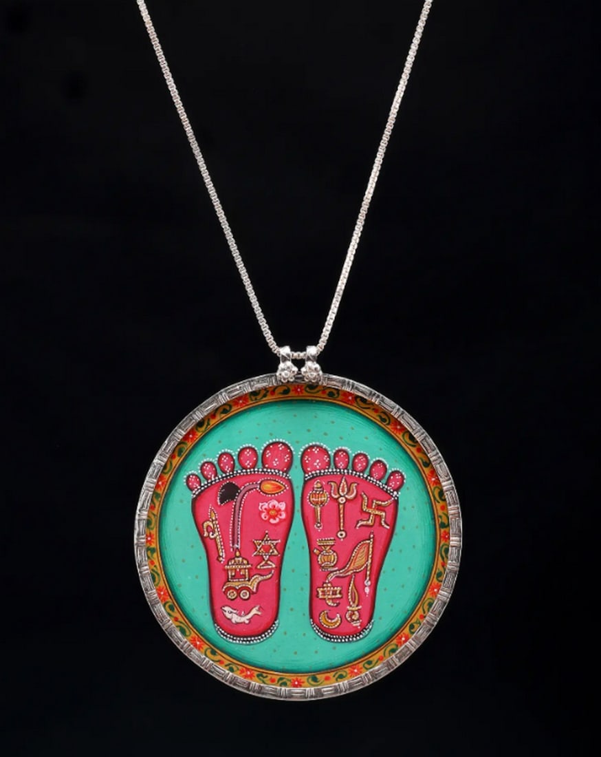 Blessings of the Lotus Pendant: Blessings of the Lotus Pendant This round pendant features the revered lotus feet, a sacred symbol in many traditions. With vibrant hand-painted details, it embodies faith and artistry. A meaningful