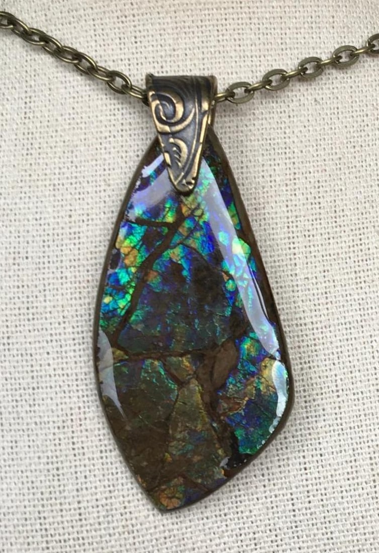 Midnight Umber Ammolite Pendant: Midnight Umber Ammolite Pendant This ammolite pendant features a gem in deep blue and umber, with occasional brighter flecks. The stone has a more subdued, earthy appearance, making it an ideal choic