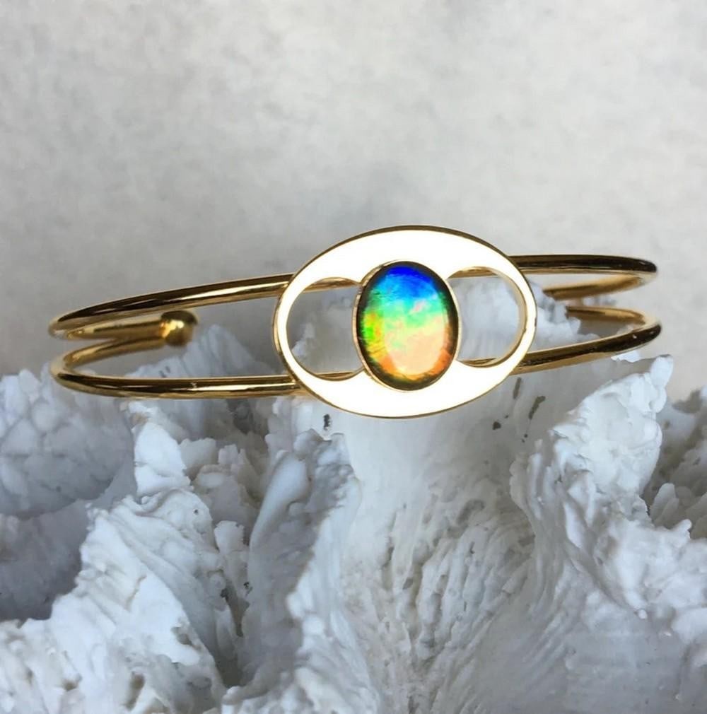 Celestial Tide Ammolite Cuff Bracelet: Celestial Tide Ammolite Cuff Bracelet This cuff bracelet features a 10mm x 8mm multi-colored gemstone, adding a striking touch to the design. It sits comfortably on a slender wrist and is crafted from