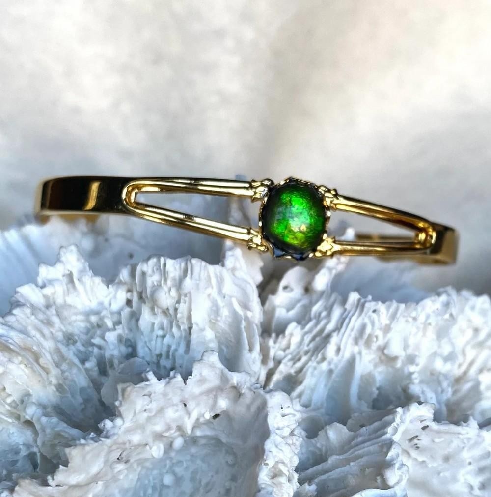 Enchanted Moss Ammolite Cuff: Enchanted Moss Ammolite Cuff This cuff bracelet features a freeform ammolite gemstone set in a sturdy gold-plated base metal. Designed for comfort, it sits well on a slender wrist. Ammolite is believe