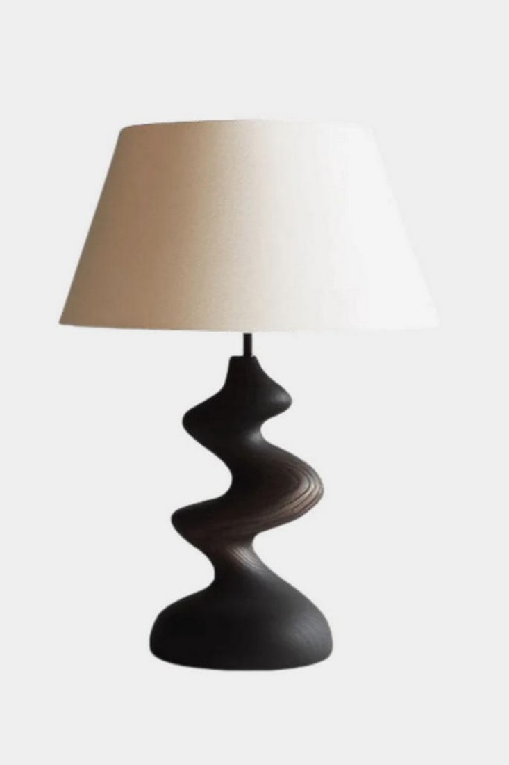 Wavy Contour Wooden Table Lamp: Wavy Contour Wooden Table Lamp Artistic and modern, this handcrafted table lamp features a sculptural base with a flowing, undulating form in a deep, smooth finish. The dynamic silhouette evokes movem