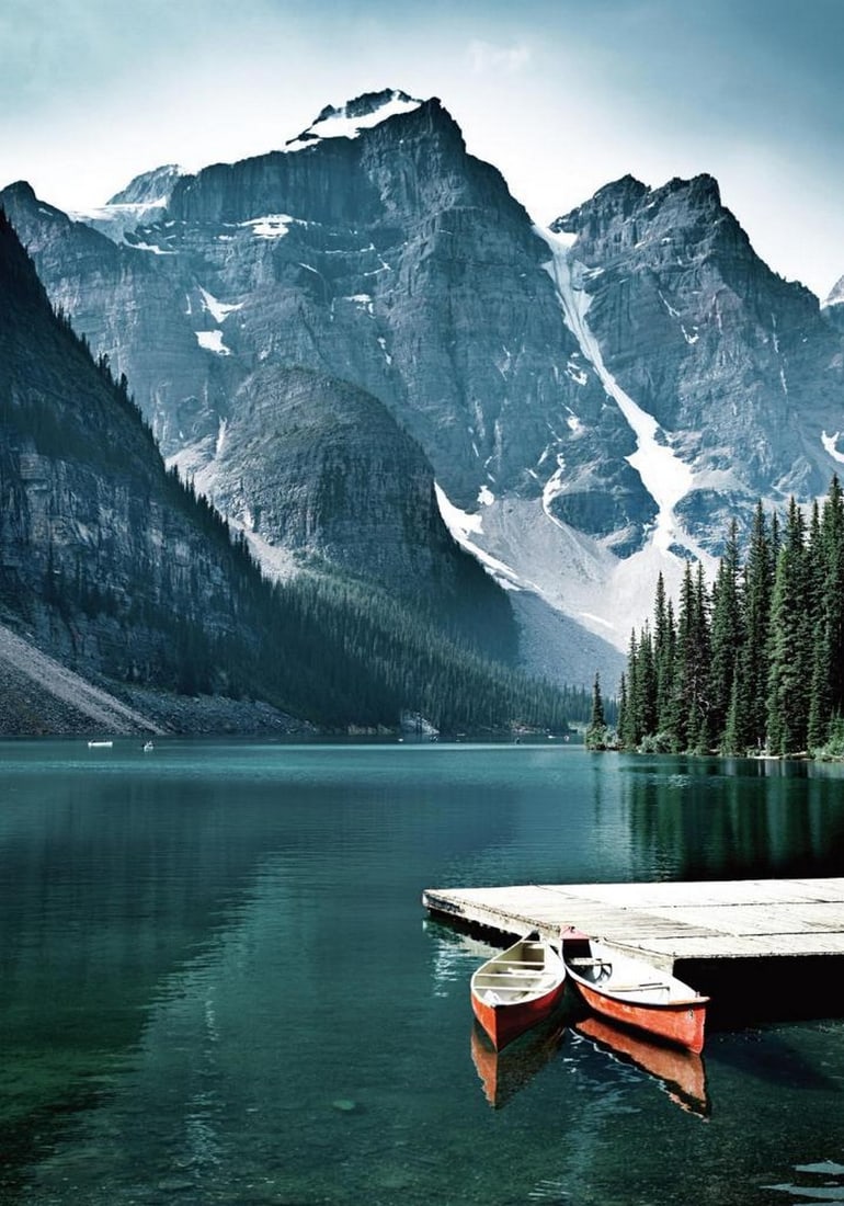 Mountain Lake Canoes Poster: Mountain Lake Canoes Poster A photographic print featuring two red canoes resting on a wooden pier along a tranquil lake. Towering, snow-covered mountains line the shore, beautifully reflected on the