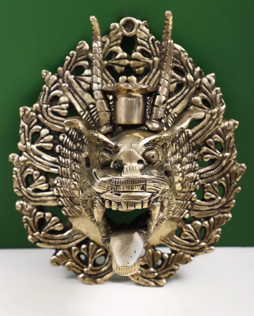 7" Brass Yamantaka Mask Wall-Hanging Candle Stand: 7" Brass Yamantaka Mask Wall-Hanging Candle Stand Wall-hanging candle stand made from brass, featuring a Yamantaka mask design. The piece includes a holder for a small candle and can be mounted o