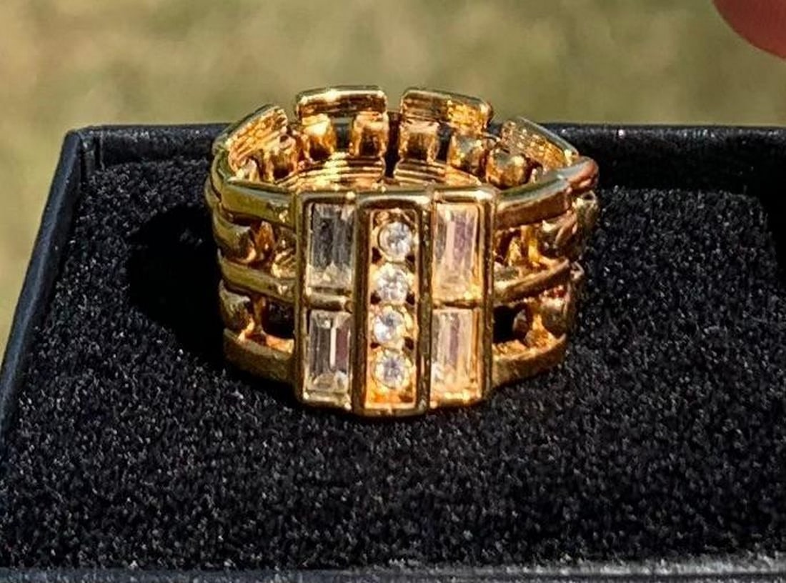 Chain-Link Ring with White Crystal Accents: Chain-Link Ring with White Crystal Accents This stylish gold-colored ring features a unique chain-link design, reminiscent of a sleek watch band, offering a bold yet sophisticated look. The front of