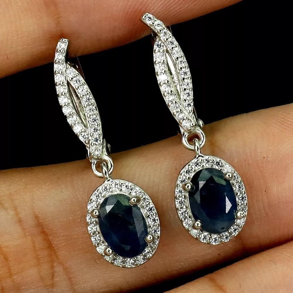 Sterling Silver Dangle Earrings with Oval Blue Sapphire Gemstones: Sterling Silver Dangle Earrings with Oval Blue Sapphire Gemstones These elegant sterling silver earrings feature 7x5mm oval blue sapphires, radiating timeless beauty and sophistication. The deep blue