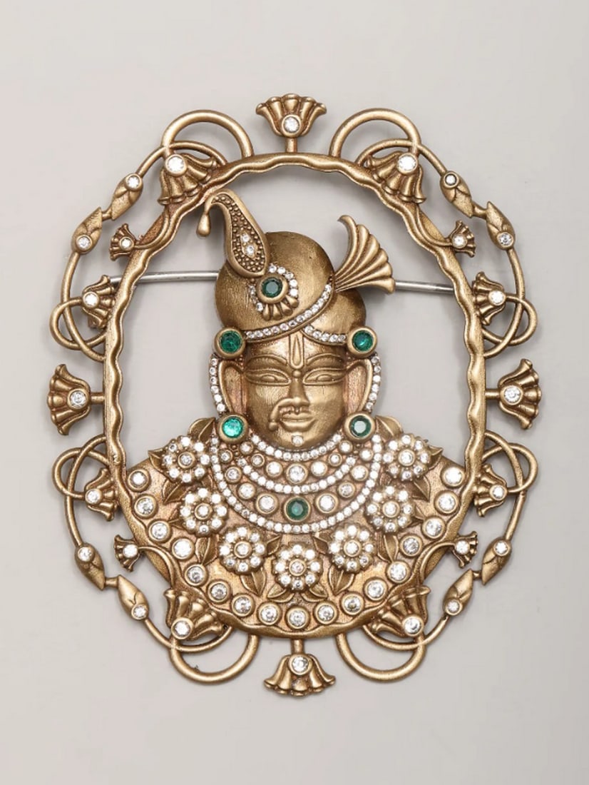 Shrinathji Stone Enchantment Brooch: Shrinathji Stone Enchantment Brooch This exquisite Shrinathji brooch, crafted from high-quality brass and adorned with sparkling stones, blends devotion with elegance. The detailed depiction of Shrina