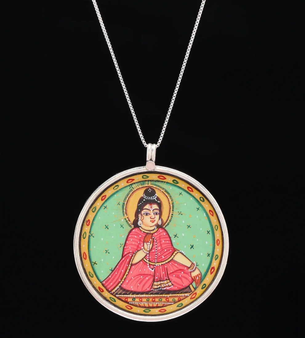Celestial Parvati Devotion Pendant: Celestial Parvati Devotion Pendant This hand-painted pendant captures Goddess Parvati in serene meditation, symbolizing devotion and feminine divinity. The vibrant colors, inspired by traditional