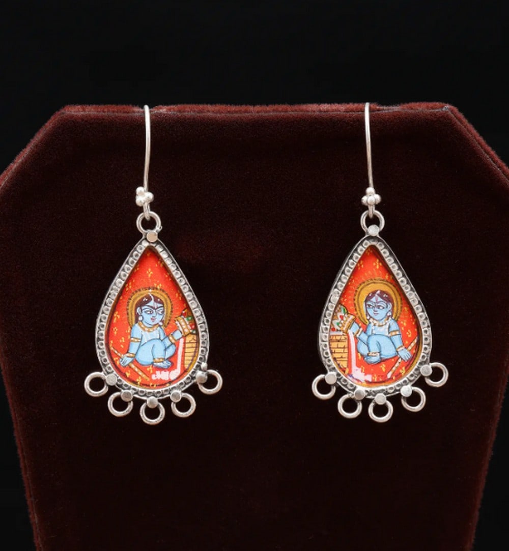 Sterling Grace Krishna Earrings: Sterling Grace Krishna Earrings These teardrop-shaped earrings blend artistry and spirituality, featuring a hand-painted miniature of Lord Krishna set in sterling silver. Vibrant colors and