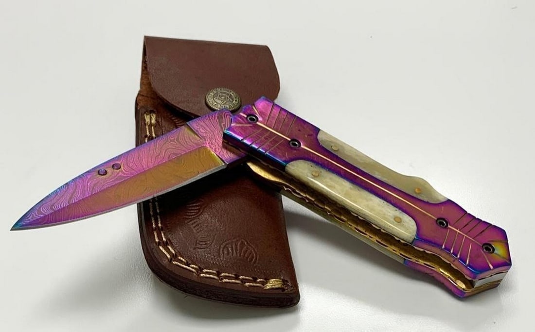 Tamascus Style Rainbow Blade Flip Knife With Leather Sheath: Tamascus Style Rainbow Blade Flip Knife With Leather Sheath Introducing our Damascus Steel Blade, a true work of art with a mesmerizing pattern formed by 256 layers of precision-crafted steel.