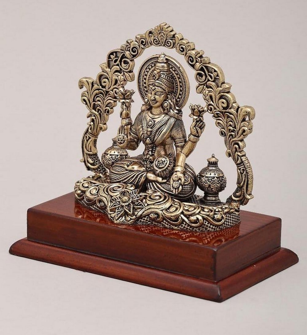 5" Four-Armed Dhanalakshmi on Wooden Base: 5" Four-Armed Dhanalakshmi on Wooden Base This 5" brass idol beautifully depicts Goddess Lakshmi, the deity of wealth, fortune, and prosperity, seated with her four arms, each symbolizing div