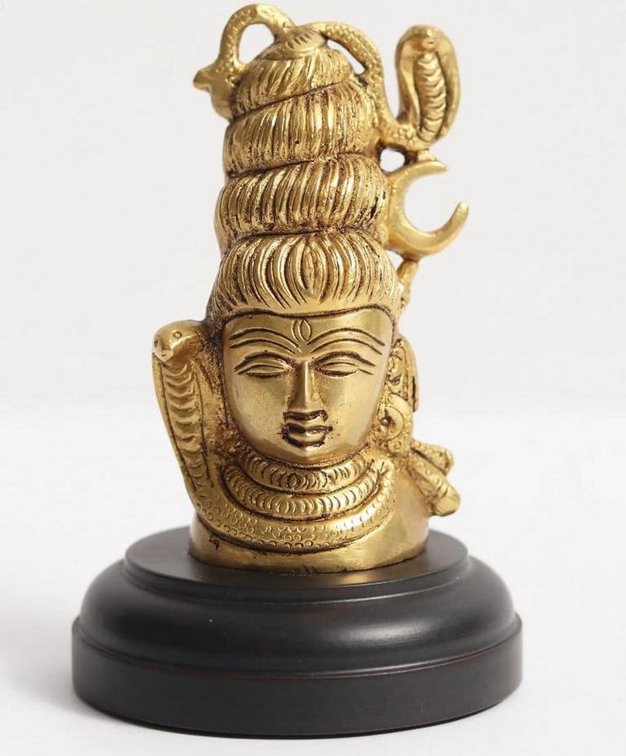 4" Small Brass Shiva Head on Wooden Base: 4" Small Brass Shiva Head on Wooden Base This 4" brass sculpture beautifully depicts the serene and powerful visage of Lord Shiva, one of Hinduism’s principal deities. The upper portion of
