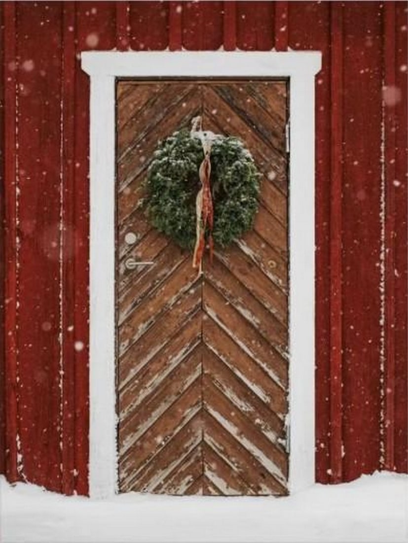 Winter Wreath Door Canvas Print: Winter Wreath Door Canvas Print An artwork showing a festive wooden door with a wreath on a red wall, surrounded by falling snow. The composition captures a cozy winter scene with a subtle grainy tex