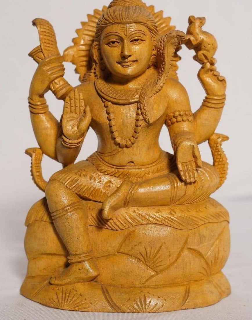 9" Four-Armed Mahadeva Sculpture Handmade White Wood Figurine: 9" Four-Armed Mahadeva Sculpture Handmade White Wood Figurine This finely handcrafted statue depicts Lord Shiva (Mahadeva) with four arms, seated in meditation on a stylized lotus base. Carved