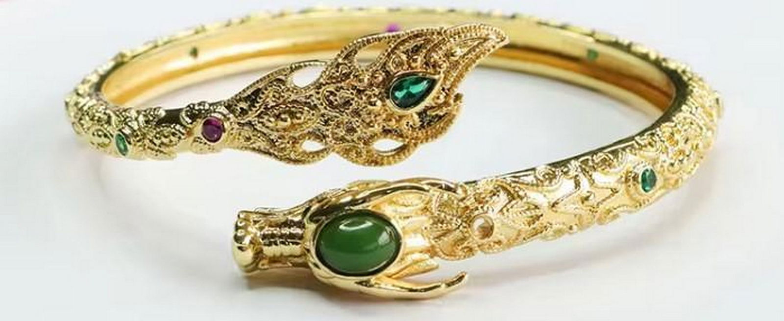 Dragon Head Bangle with Green Stones: Dragon Head Bangle with Green Stones This enchanting gold-tone bracelet showcases twin dragon heads, symbolizing strength and protection. Set with shimmering green stones, it blends mythical charm