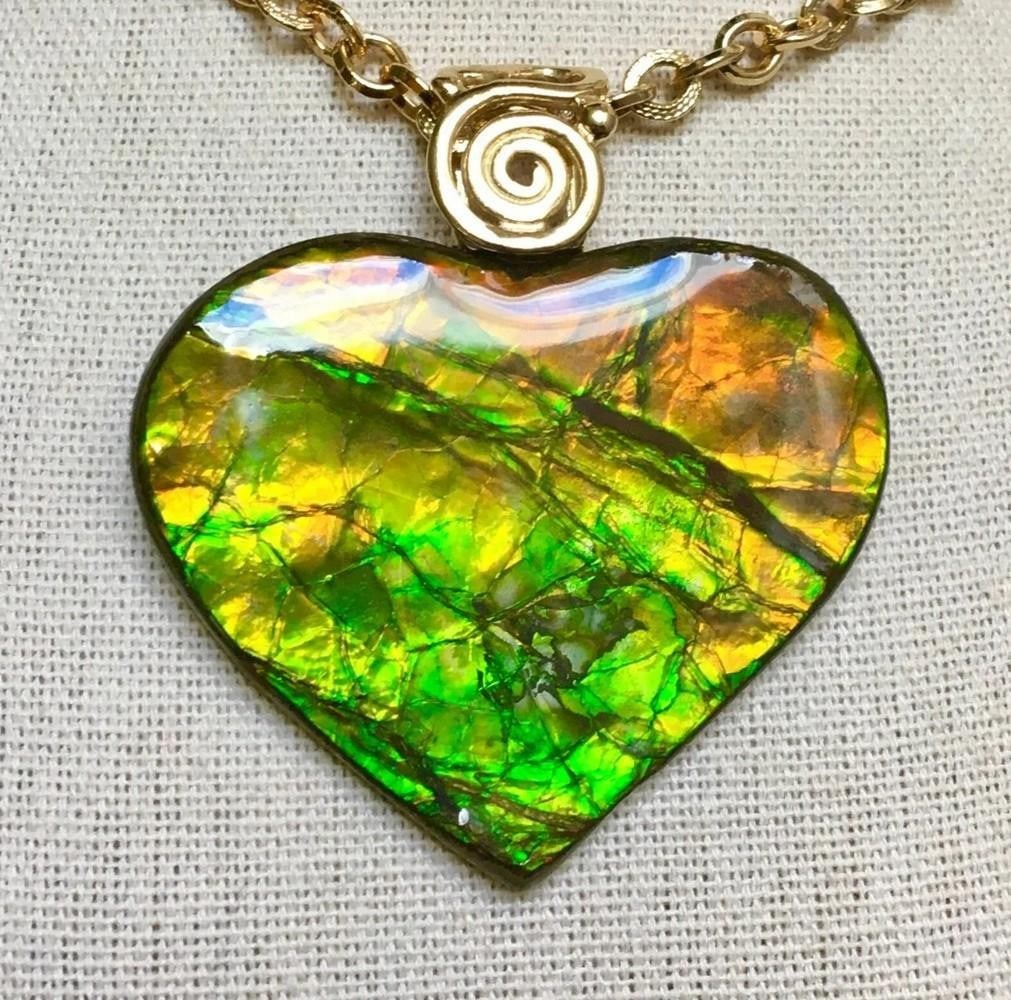 Autumn Heart Ammolite Pendant: Autumn Heart Ammolite Pendant This ammolite pendant features a large heart-shaped gem in green and orange, which shifts to green with hints of teal at extreme angles. The stone has a smooth resin