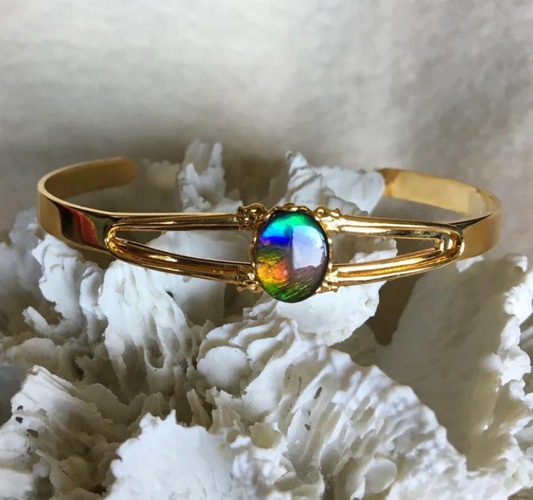 Iridescent Earth Ammolite Cuff Bracelet: Iridescent Earth Ammolite Cuff Bracelet This cuff bracelet features a 10mm x 8mm multi-colored gemstone, offering a vibrant and eye-catching display. It sits comfortably on a slender wrist and is
