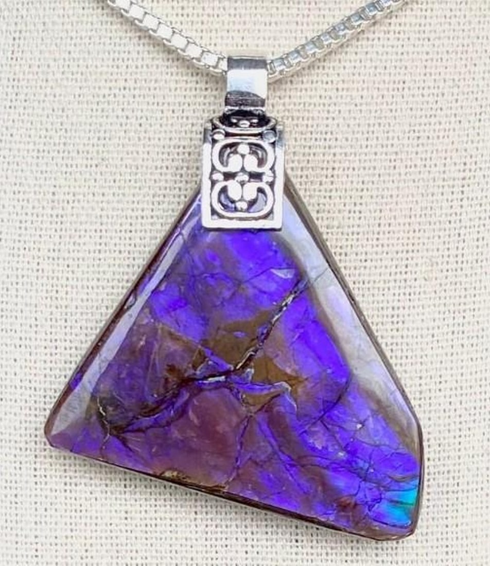 Twilight Aura Ammolite Pendant: Twilight Aura Ammolite Pendant The Twilight Aura Ammolite Pendant shimmers with enchanting shades of violet, reflecting the mystery and allure of dusk. Its natural iridescence shifts with the
