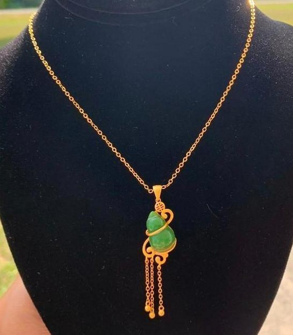 Gold & Jade Pendant Necklace: Gold & Jade Pendant Necklace This elegant necklace features a stunning jade stone pendant, beautifully complemented by delicate gold colored accents. The jade is wrapped in intricate gold