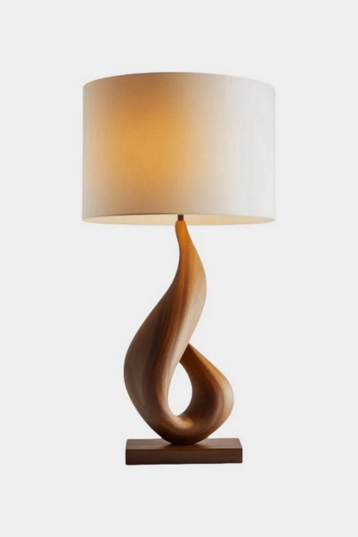Wood Twisted Loop Lamp: Wood Twisted Loop Lamp This table lamp features a cylindrical white shade set above a sculptural wooden base shaped into a smooth, twisting loop. The form introduces a sense of movement while