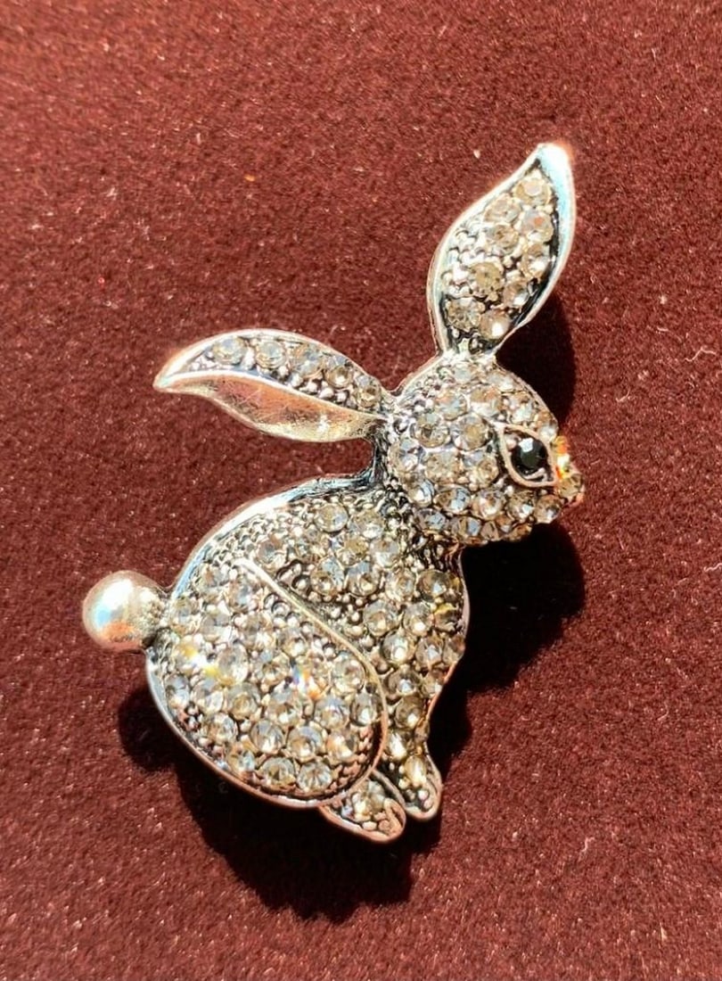 Radiant Bunny Brooch: Radiant Bunny Brooch This playful brooch showcases a charming bunny sitting elegantly, its body adorned with shimmering rhinestones that catch the light with every movement. The bunny’s ears