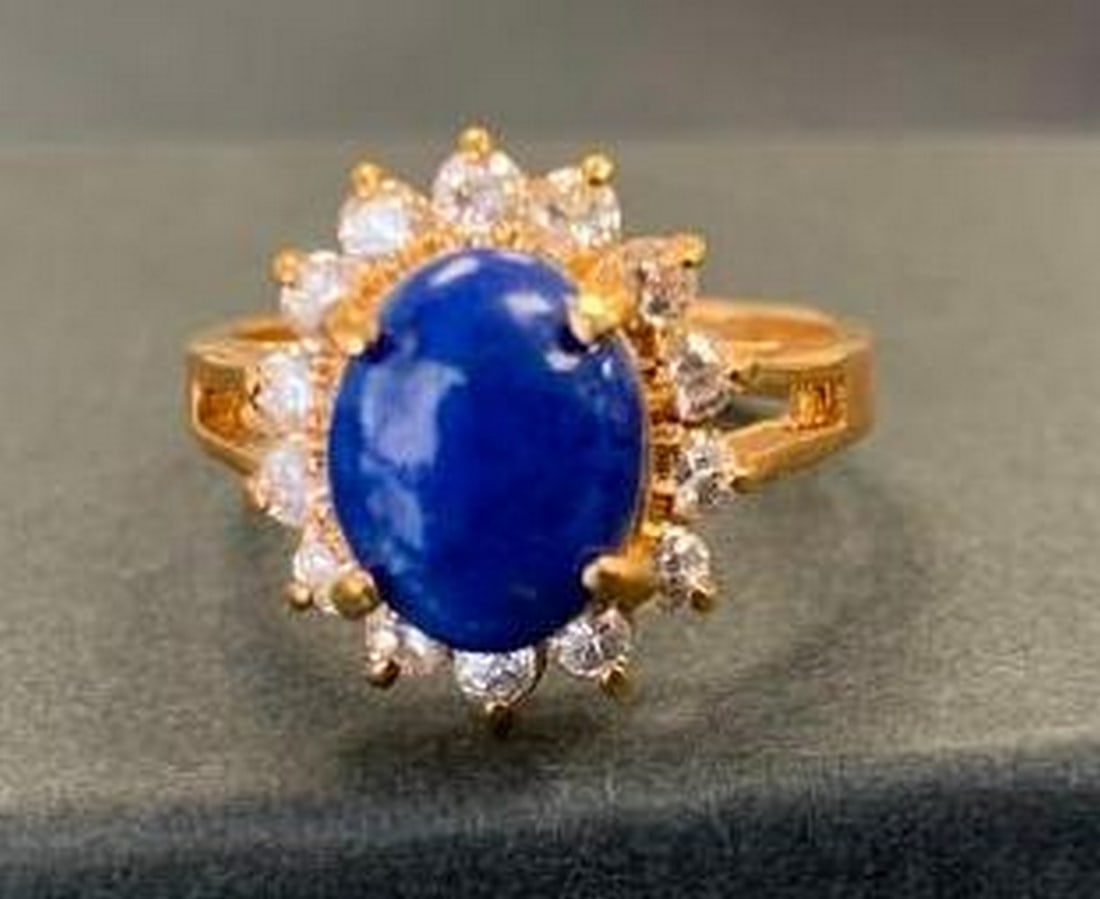 18K Gold Electroplated Ring with Blue Oval Stone: 18K Gold Electroplated Ring with Blue Oval Stone A timeless statement piece, this 18K gold electroplated ring features a brilliant blue oval stone at its center, surrounded by a sparkling halo of cle