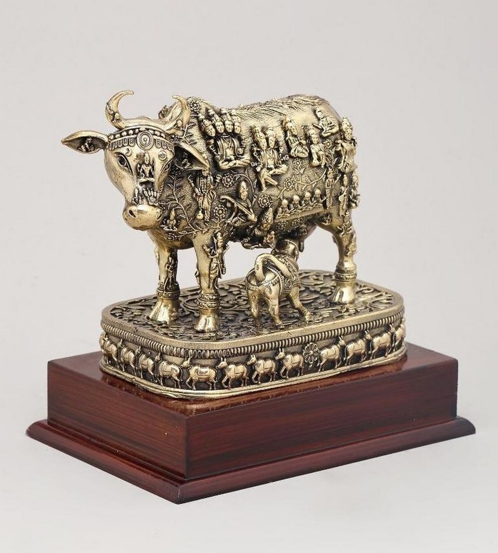 8" Kamdhenu Cow and Calf on Wooden Base: 8" Kamdhenu Cow and Calf on Wooden Base This 8" brass figurine beautifully depicts Kamdhenu, the divine wish-fulfilling cow, with her calf, on a wooden base. Intricate engravings of many Hind