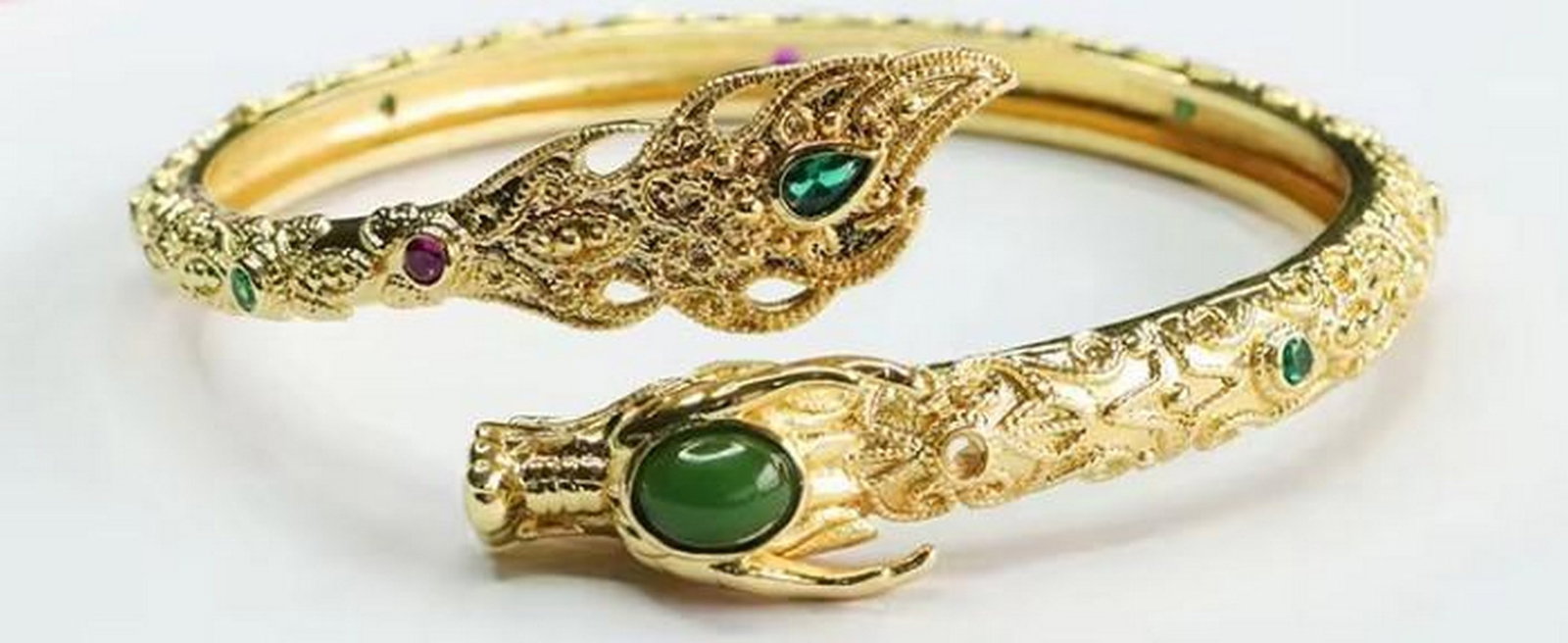Dragon Head Bangle with Green Stones: Dragon Head Bangle with Green Stones This enchanting gold-tone bracelet showcases twin dragon heads, symbolizing strength and protection. Set with shimmering green stones, it blends mythical charm wit