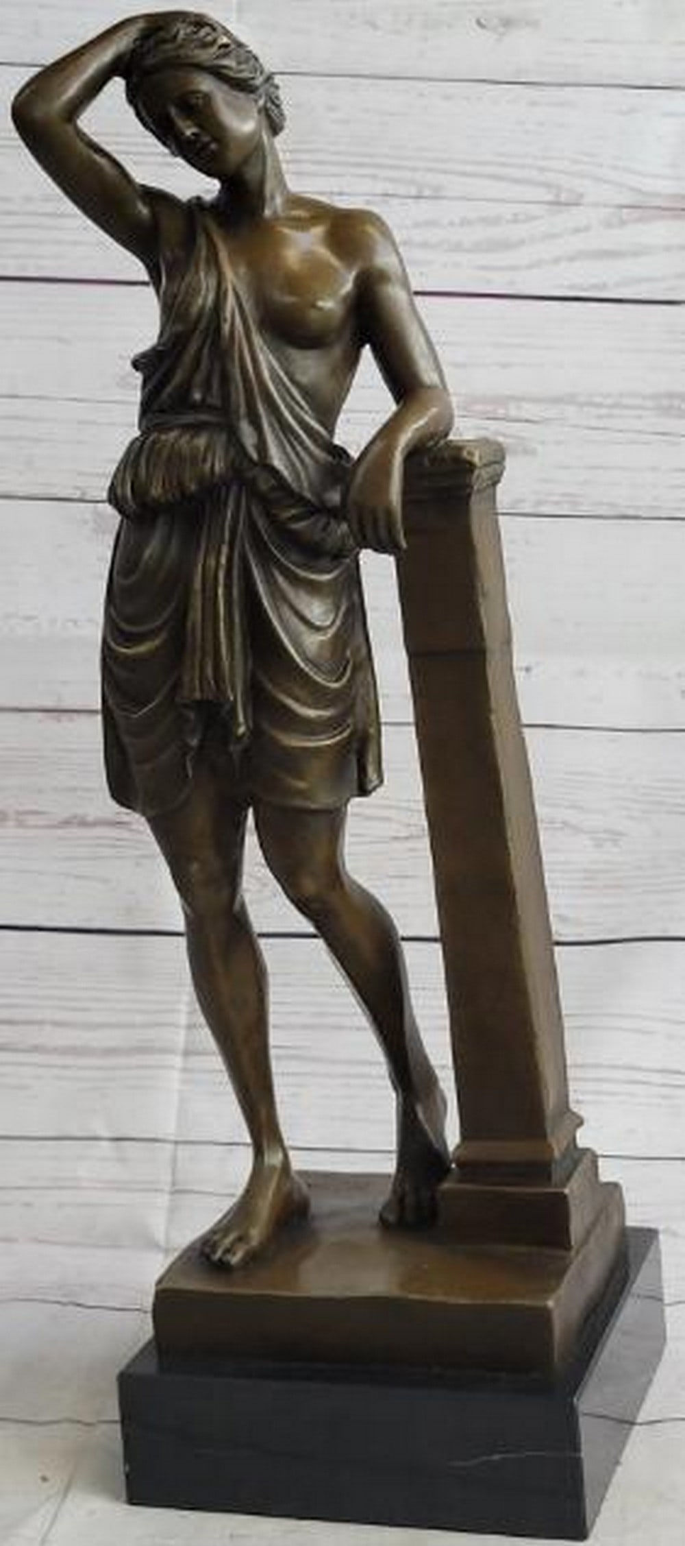 Goddess in Repose Bronze Sculpture: Goddess in Repose Bronze Sculpture This elegant reproduction bronze sculpture captures a semi-nude goddess in a moment of relaxed grace, leaning thoughtfully against a classical pillar. Her elbow res