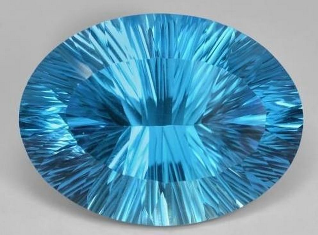 Swiss Blue Topaz Oval Concave Cut Gemstone: Swiss Blue Topaz Oval Concave Cut Gemstone Brilliantly faceted with a modern oval concave cut, this Swiss Blue Topaz dazzles with vibrant, crystal-clear color and exceptional light play. The dynamic