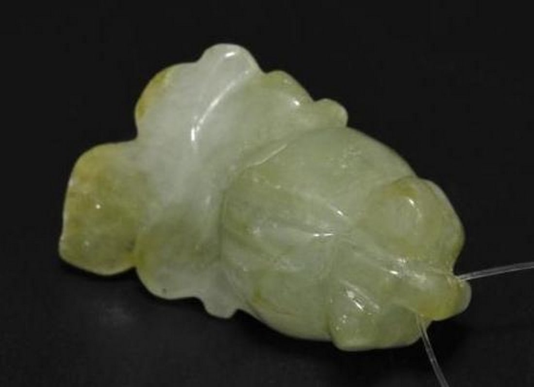 Warm Green Jade Carved Fish Gemstone: Warm Green Jade Carved Fish Gemstone This exquisite loose gemstone is carved from warm green jade into the graceful shape of a fish, complete with finely detailed features. A 0.65 mm drilled hole add