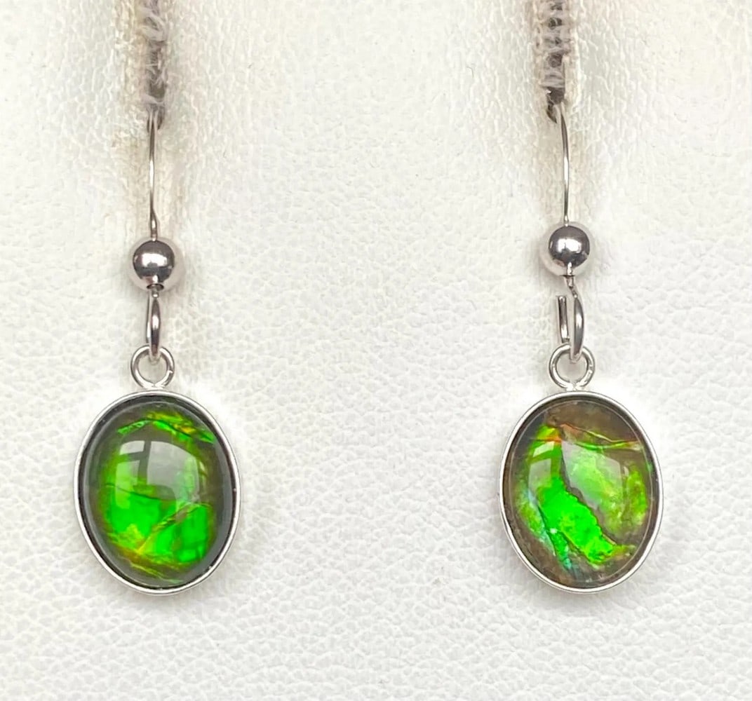 Green Oval Cut Ammolite Earrings: Green Oval Cut Ammolite Earrings These Ammolite earrings showcase a rich green hue with a beautifully textured crinkled pattern. The 10mm x 8mm medium-dome quartz-capped triplets are set in