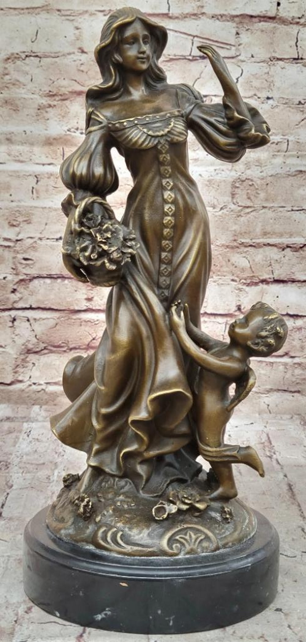 Women Standing with Winged Cherub - 15" x 6.5": Women Standing with Winged Cherub - 15" x 6.5" This enchanting sculpture features a beautiful young woman resting by a meadow, accompanied by a baby angel who adores her. He stands beside her,