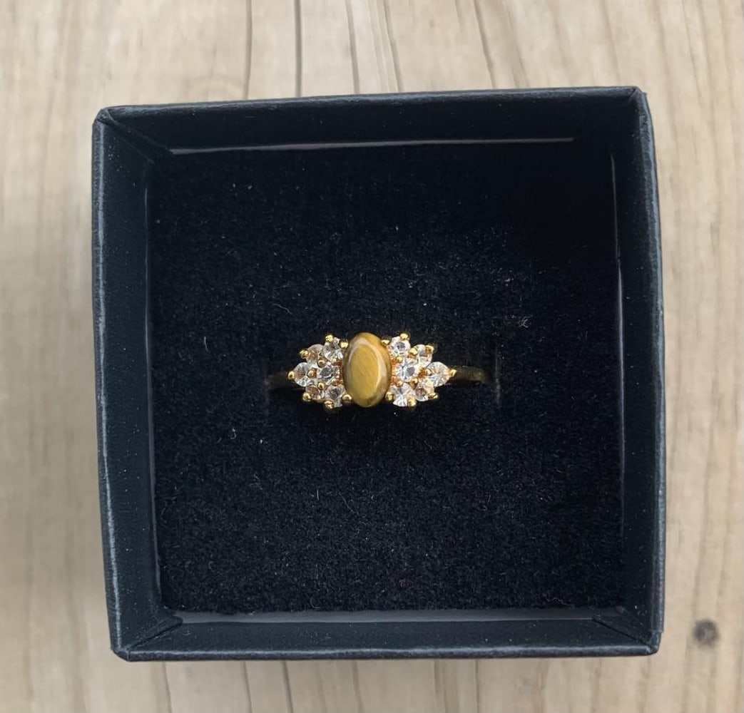 Golden Gaze Ring: Golden Gaze Ring This classic ring features an oval-cut tiger’s eye gemstone, prized for its golden-brown bands and natural chatoyancy. Set in a warm gold-tone band, the stone shimmers with depth an
