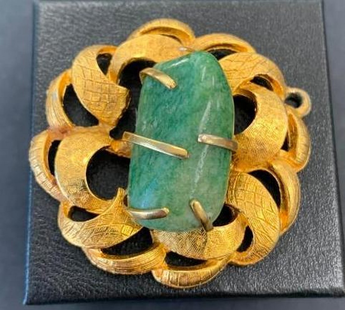 Circle Pendant with Jade Center: Circle Pendant with Jade Center This elegant gold-tone pendant features a circular ribbon-like design with graceful cut-out twists that create a sense of movement and light. At its center rests a poli