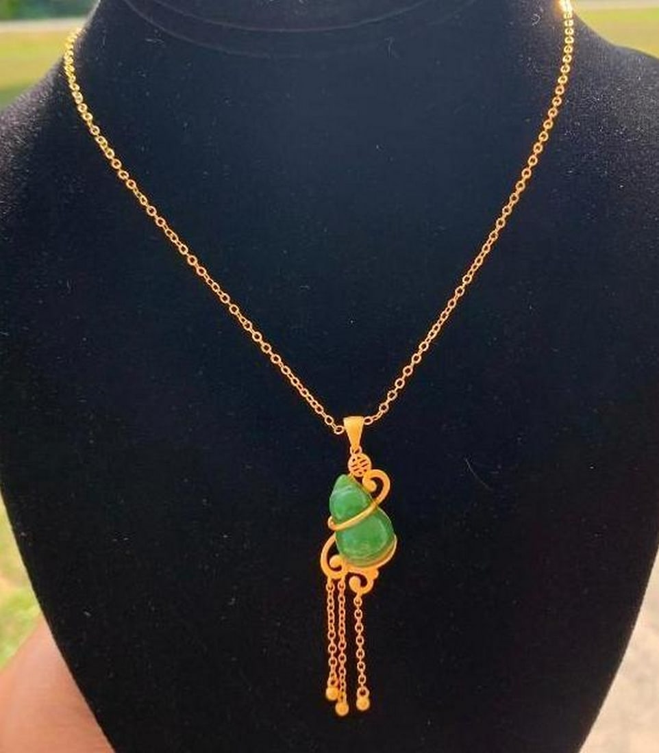 Gold & Jade Pendant Necklace: Gold & Jade Pendant Necklace This elegant necklace features a stunning jade stone pendant, beautifully complemented by delicate gold colored accents. The jade is wrapped in intricate gold colored
