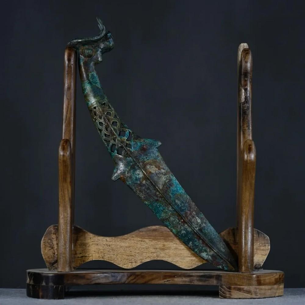 Antique Chinese Sheep Head Bronze Dagger Ornament: Antique Chinese Sheep Head Bronze Dagger Ornament This antique Chinese bronze dagger ornament showcases a meticulously detailed sheep head motif, symbolizing harmony, prosperity, and protection. The s