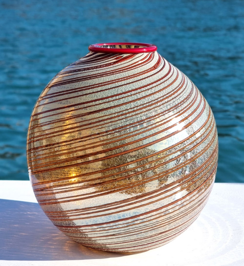 Romano Red Rim Vase with Silver Leaf Murano Glass: Romano Red Rim Vase with Silver Leaf Murano Glass This handmade Murano glass vase features a red rim and silver leaf decoration. Crafted by skilled artisans in Murano, the vase combines transparent gl