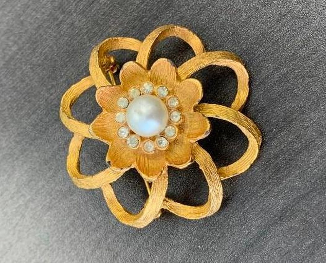 Gold-Tone Floral Brooch with Pearl Center: Gold-Tone Floral Brooch with Pearl Center This elegant flower-shaped brooch features a luminous central pearl encircled by a ring of sparkling gemstones, creating a radiant focal point. The layered pe