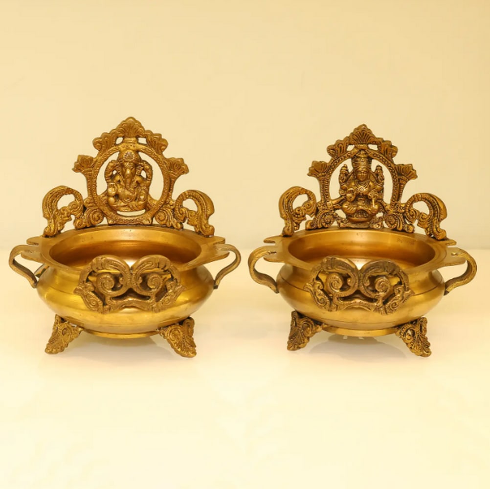 6.5" Ganesha Lakshmi Urli (Pair): 6.5" Ganesha Lakshmi Urli (Pair) Crafted from brass, this pair of Urlis features the divine forms of Lord Ganesha and Goddess Lakshmi. The bowls are designed for traditional use, often filled with