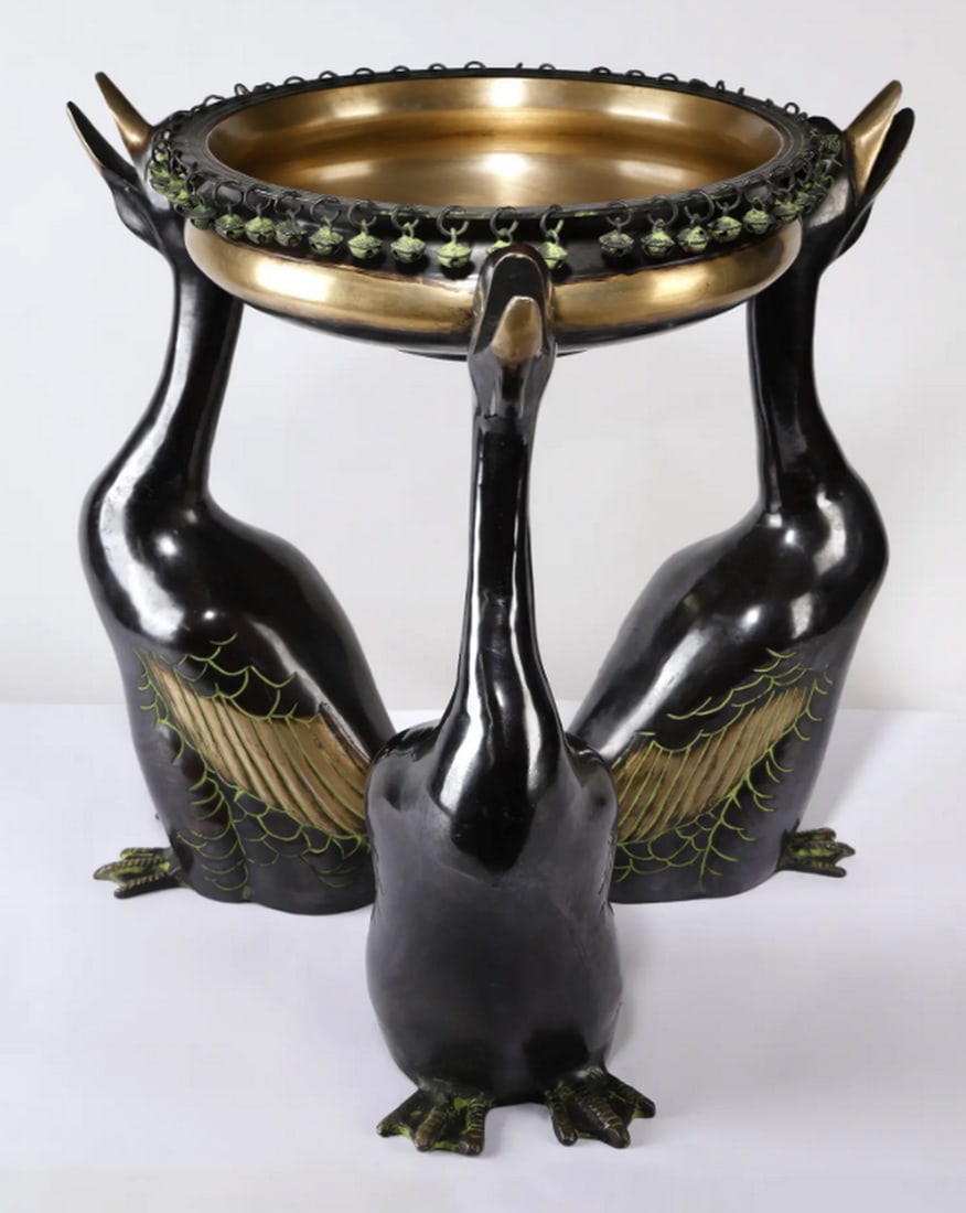 Brass Serenade (Ducks Design Brass Urli with Diya): Brass Serenade (Ducks Design Brass Urli with Diya) Designer brass urli supported by three naturalistic duck figures, each with detailed feathers, webbed feet, and open beaks. The circular urli bowl fe