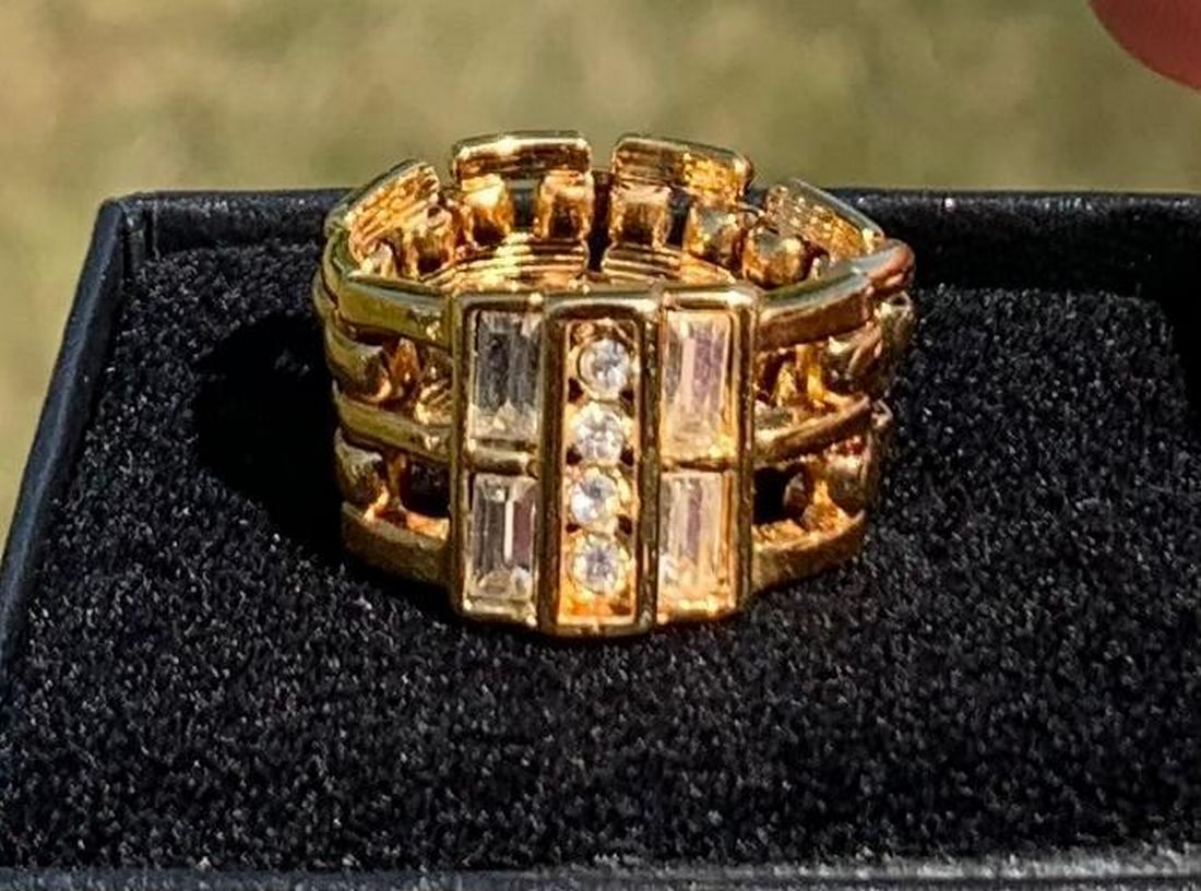 Chain-Link Ring with White Crystal Accents: Chain-Link Ring with White Crystal Accents This stylish gold-colored ring features a unique chain-link design, reminiscent of a sleek watch band, offering a bold yet sophisticated look. The front of t