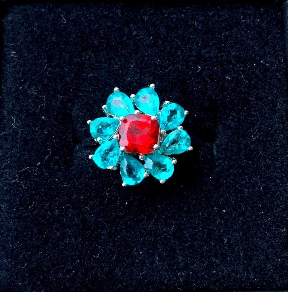 Sterling Silver Flower Ring with Blue Petal Stones: Sterling Silver Flower Ring with Blue Petal Stones Inspired by the beauty of a blooming flower, this sterling silver ring features vibrant blue stones shaped into delicate petals surrounding a bold re