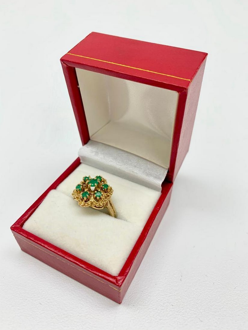 .12ct Round Cut Emerald set in 14K Gold Ring: The main stone of this piece is a .12ct round cut Emerald, which is surrounded by 6 .03ct round cut Emerald stones 