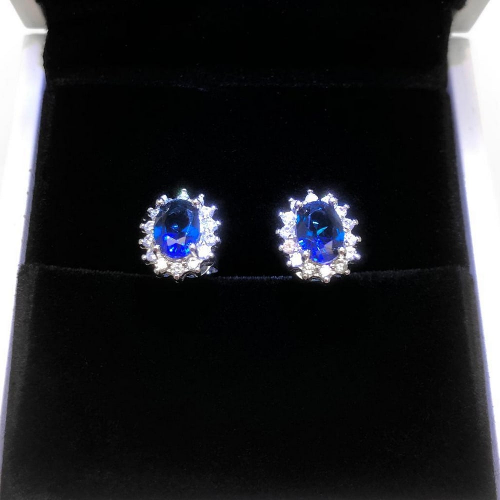 Tanzanite Stud Earrings with White Crystal Halo: Tanzanite Stud Earrings with White Crystal Halo These exquisite stud earrings feature a vibrant blue tanzanite gemstone at the center, surrounded by a sparkling halo of small white crystals. The