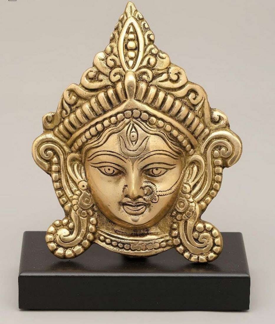 8" Handmade Brass Devi Durga Face on Wooden Stand: 8" Handmade Brass Devi Durga Face on Wooden Stand This handcrafted statue features the serene face of Devi Durga, the warrior goddess, mounted on a finely carved wooden stand. Despite her role in